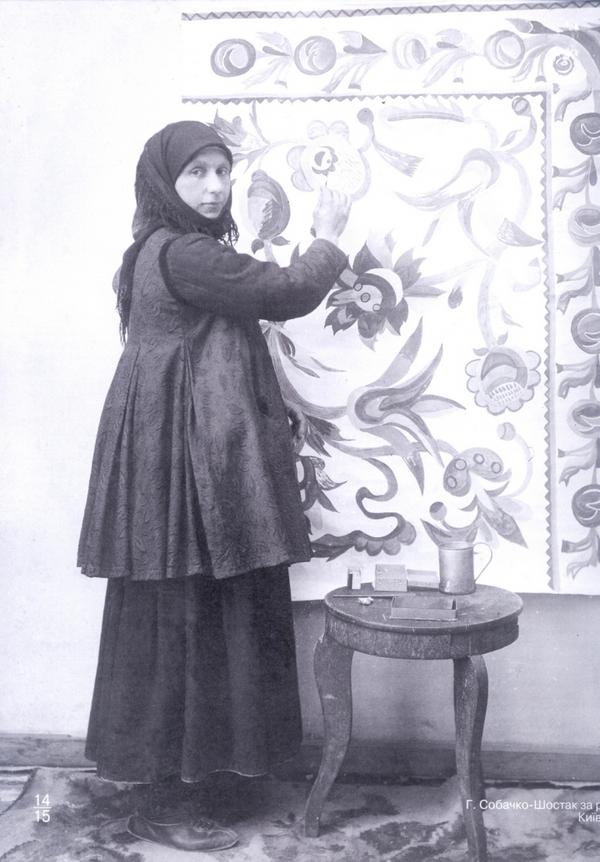 Ганна Собачко на фоні своєї роботи, с.Скопці, кустарна майстерня Семиградової, 1915.jpg